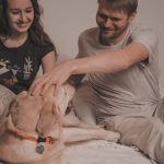 Smiling couple enjoying time with their Labrador on a bed indoors.