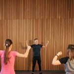 Instructor guiding two women in a gym workout session. Indoor fitness training.